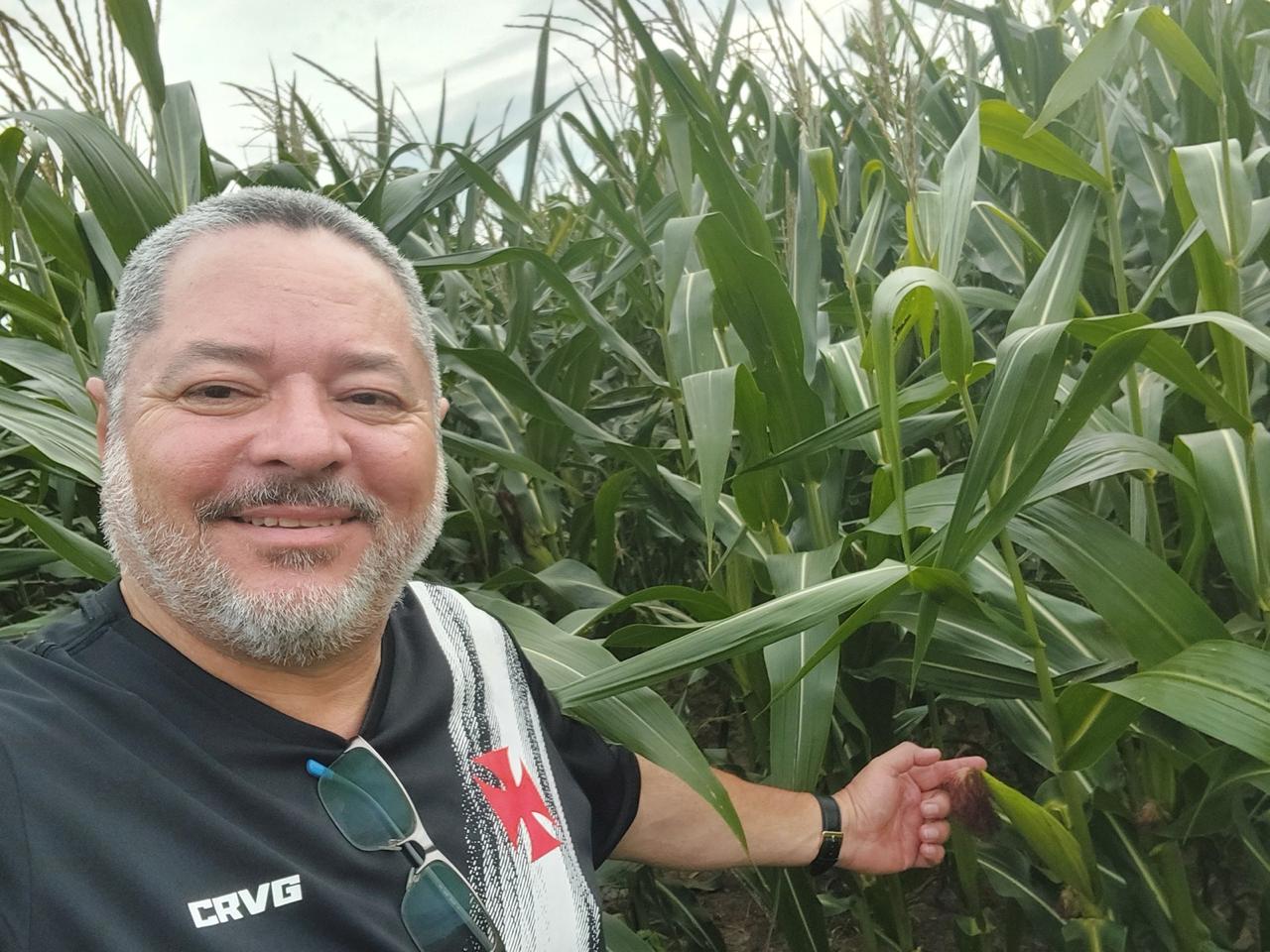 Produtor sorrindo junto aos pés de milho na plantação da fazenda