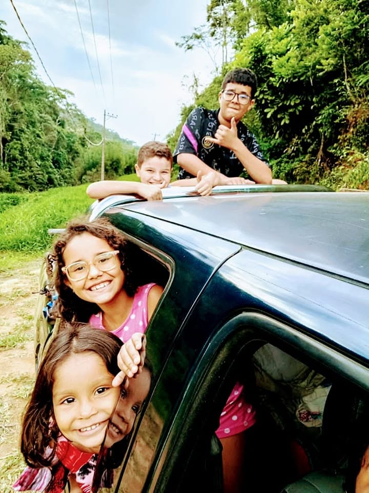 Crianças sorrindo na janela e no teto do carro em estrada de terra
