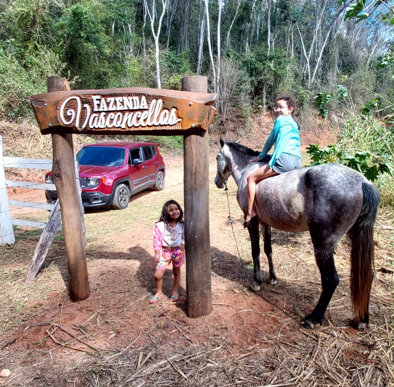 Duas netas com um cavalo sob o portal de madeira da Fazenda Vasconcellos